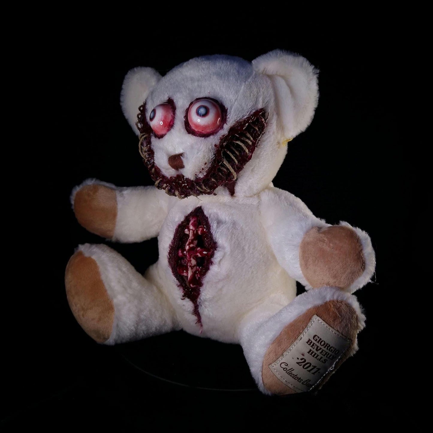 White teddy bear with bloody ribs, sewed bloody mouth and bloodshot blind eyes