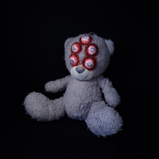Teddy bear with red bow with 5 blind eyes with blood