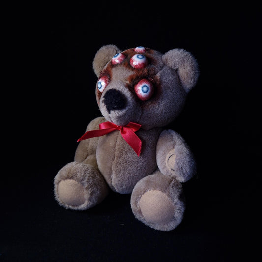 Teddy bear with red bow with 5 blind eyes with blood